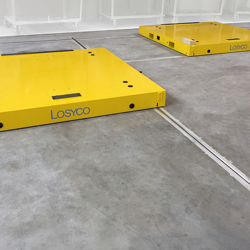 Zwei gelbe Transportplattformen der Marke Losyco auf einem Betonboden, verbunden durch in den Boden eingelassene Schienen.