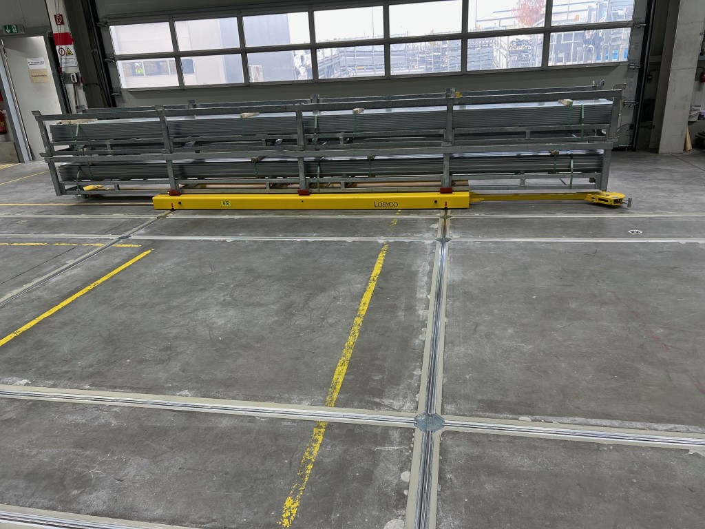 Ein großer Raum mit Betonestrichboden, der durch gelbe Linien markiert ist, zeigt eine Metallkonstruktion mit einem gelben Hebewerkzeug der Marke Losyco im Vordergrund.